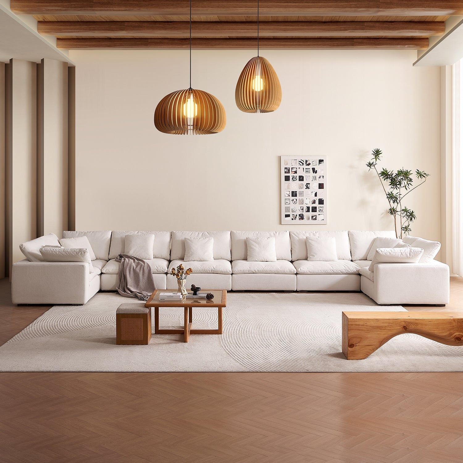 Spacious cream-colored bohemian style living room. There are wooden panel light fixtures hanging from ceiling.  In the center of the room is a coffee table, wooden bench and a throw blanket on the Tivoli cloud sectional by Mario Capasa.