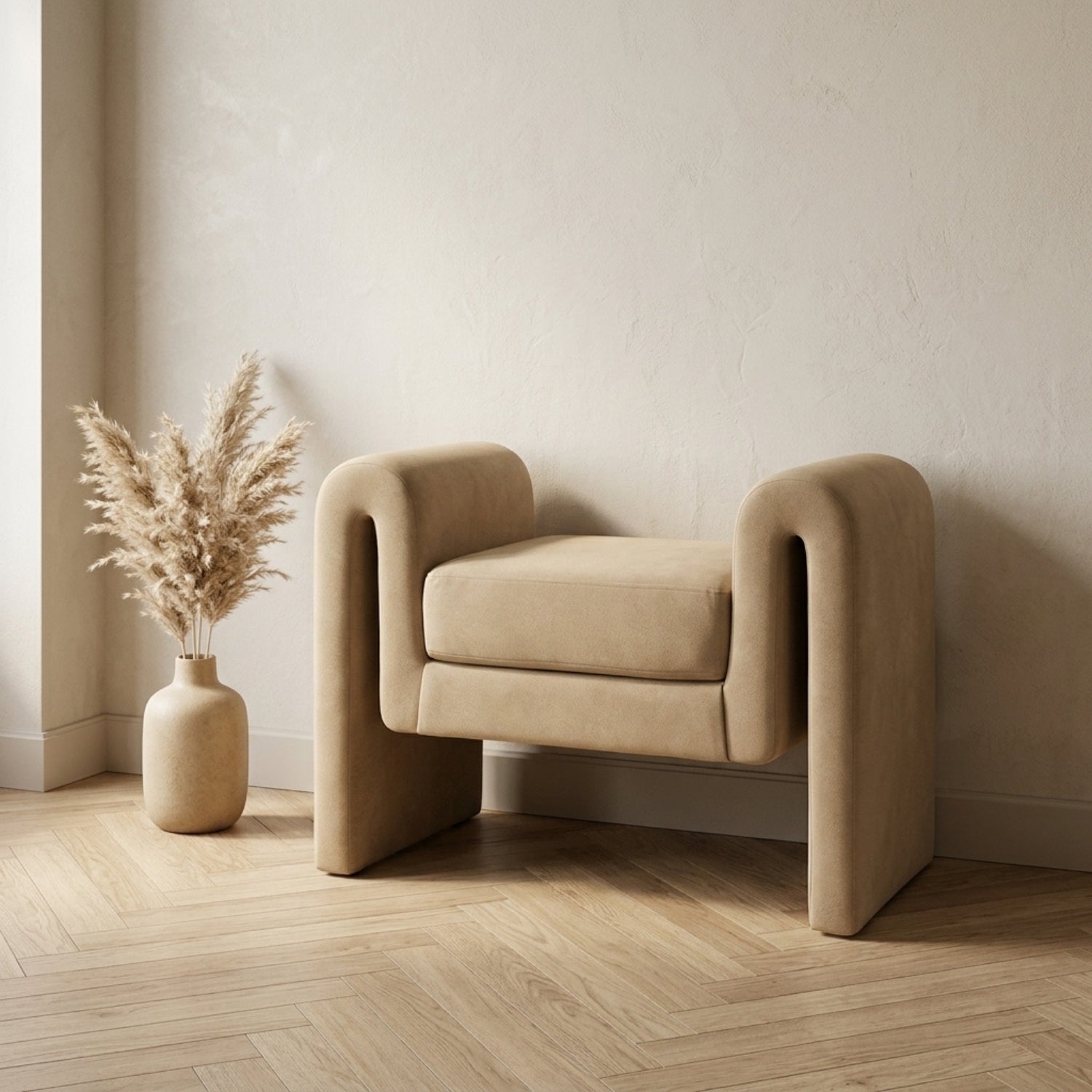 Beige armchair in a minimalistic room with a vase of dried plants on a wooden floor.