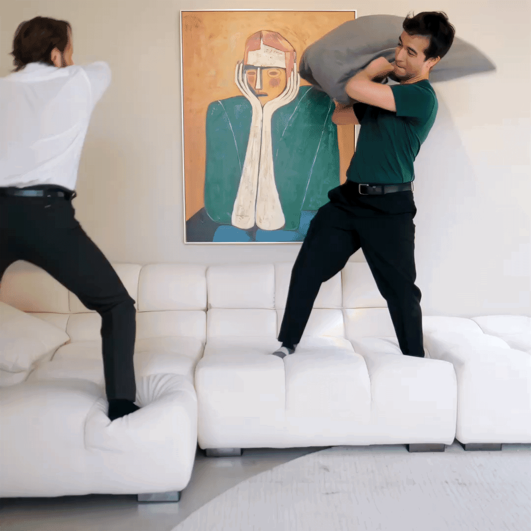 Adults laughing and jumping during a pillow fight on Mario Capasa sectional couch.
