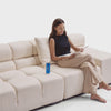 A woman sitting on a white tufted couch while reading a magazine and accidentally spills her soda on her machine washable sofa